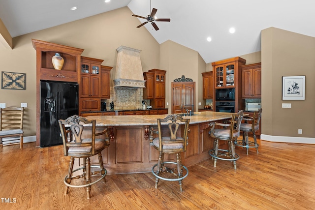 kitchen featuring light wood-type flooring, custom exhaust hood, a spacious island, and black appliances