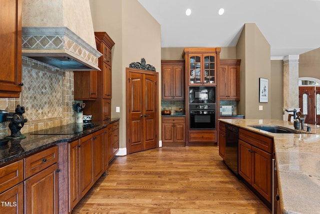 kitchen with light stone countertops, sink, light hardwood / wood-style flooring, black appliances, and custom range hood