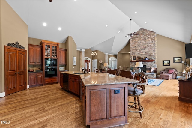 kitchen featuring a kitchen bar, a spacious island, black appliances, hardwood / wood-style flooring, and a stone fireplace