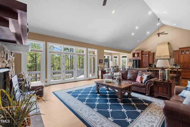 living room with a wealth of natural light, a fireplace, ceiling fan, and high vaulted ceiling