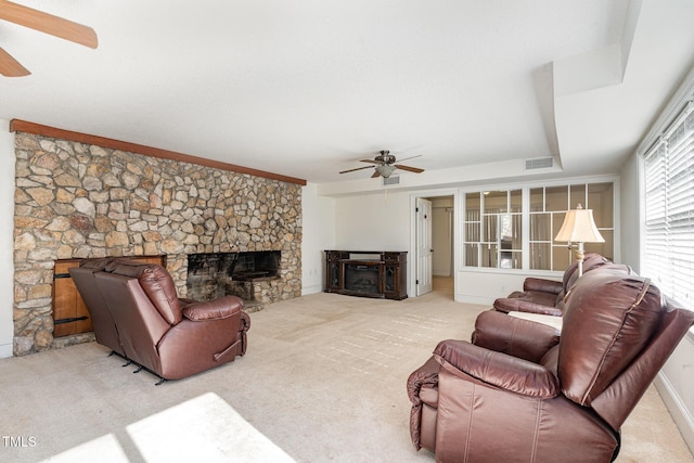 carpeted living room with ceiling fan and a stone fireplace