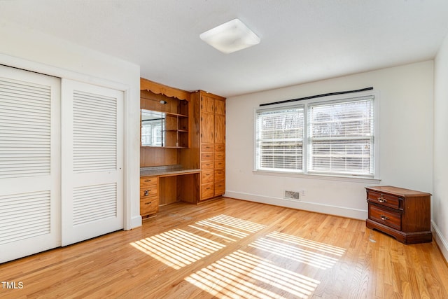 unfurnished bedroom with light wood-type flooring, a closet, and built in desk