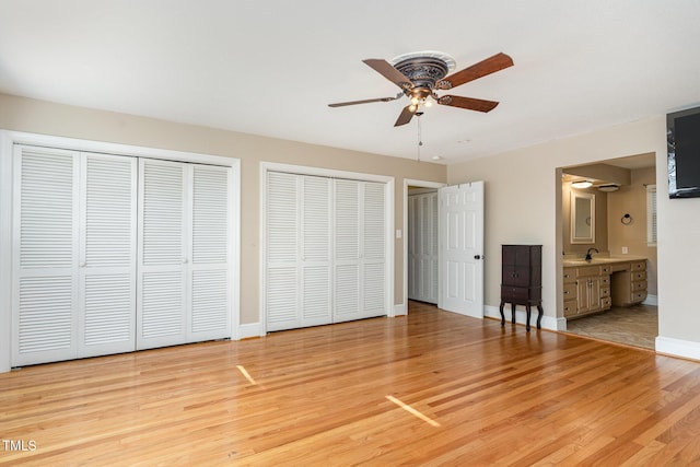 unfurnished bedroom with ceiling fan, ensuite bathroom, light hardwood / wood-style flooring, and multiple closets