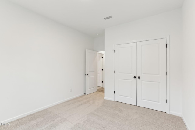 unfurnished bedroom with a closet, light carpet, and baseboards