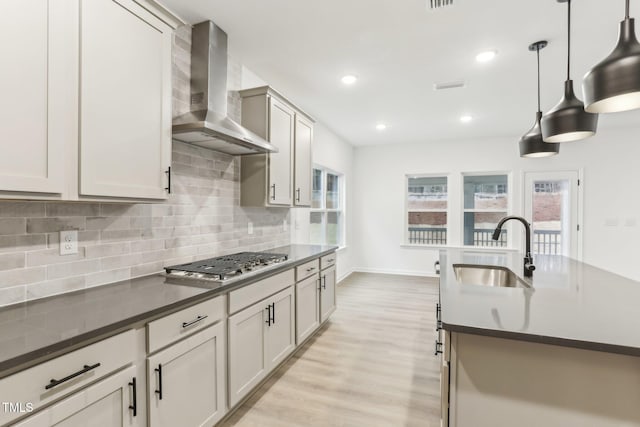 kitchen with dark countertops, stainless steel gas stovetop, wall chimney range hood, and a sink