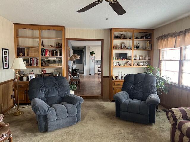 living area featuring ceiling fan, carpet, a textured ceiling, and wooden walls