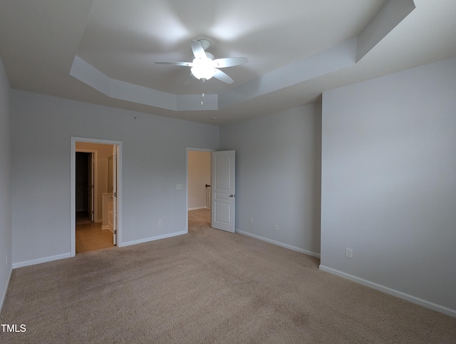 empty room with a raised ceiling, ceiling fan, and light carpet