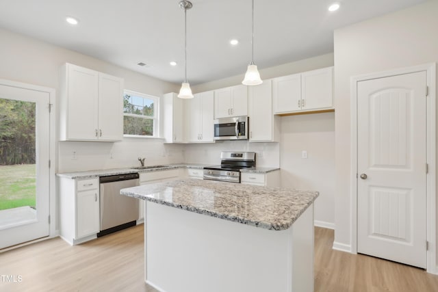 kitchen with appliances with stainless steel finishes, white cabinetry, hanging light fixtures, and a kitchen island