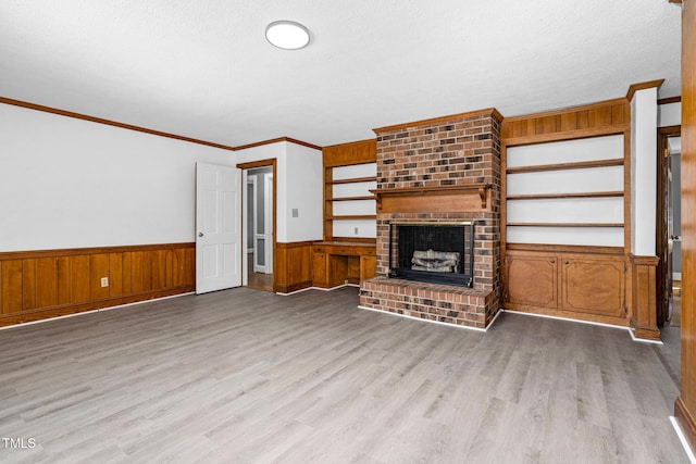 unfurnished living room with a fireplace, wood walls, crown molding, a textured ceiling, and light hardwood / wood-style flooring