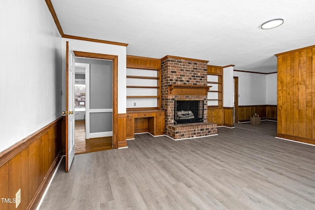 unfurnished living room featuring light hardwood / wood-style flooring, crown molding, a fireplace, and wood walls