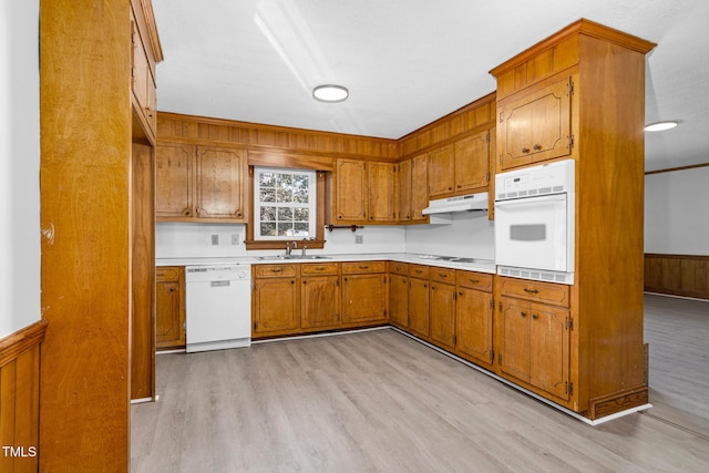 kitchen featuring sink, white appliances, wooden walls, and light wood-type flooring