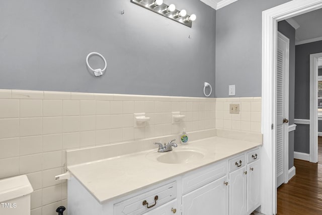 bathroom featuring wood-type flooring, tile walls, vanity, toilet, and crown molding