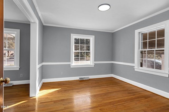 empty room featuring hardwood / wood-style flooring, ornamental molding, and a healthy amount of sunlight