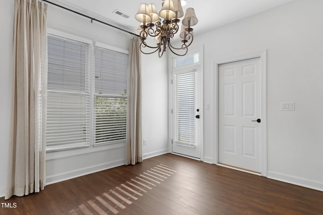 spare room with plenty of natural light, dark hardwood / wood-style floors, and an inviting chandelier