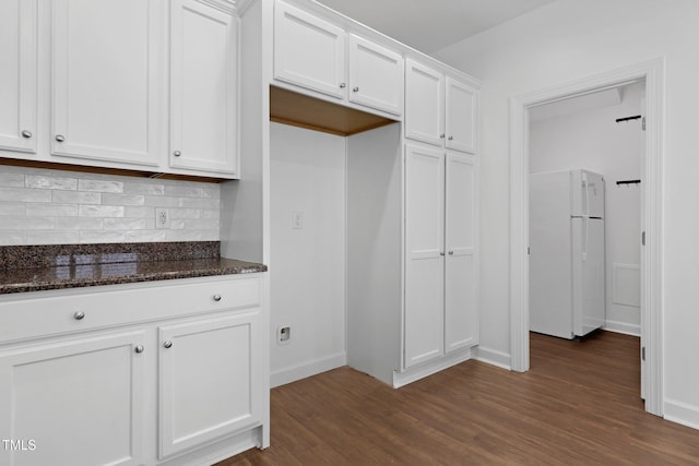 kitchen with decorative backsplash, white cabinetry, dark stone counters, and white refrigerator