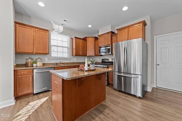 kitchen with a breakfast bar, appliances with stainless steel finishes, a center island, light stone counters, and light hardwood / wood-style floors