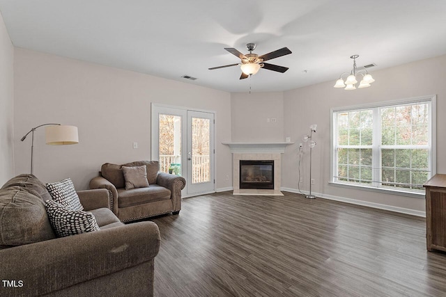 living room with dark hardwood / wood-style floors, ceiling fan with notable chandelier, and a tiled fireplace