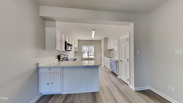 kitchen with white cabinetry, sink, kitchen peninsula, light hardwood / wood-style floors, and appliances with stainless steel finishes