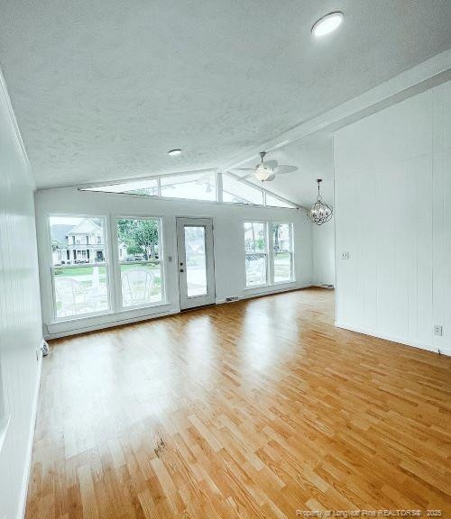 spare room featuring a textured ceiling, vaulted ceiling with beams, light wood-type flooring, and ceiling fan with notable chandelier