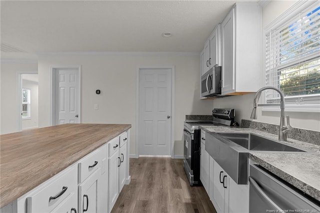 kitchen featuring hardwood / wood-style floors, stainless steel appliances, white cabinetry, and crown molding