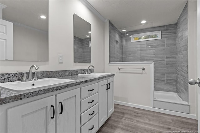 bathroom featuring wood-type flooring, vanity, a tile shower, and ornamental molding