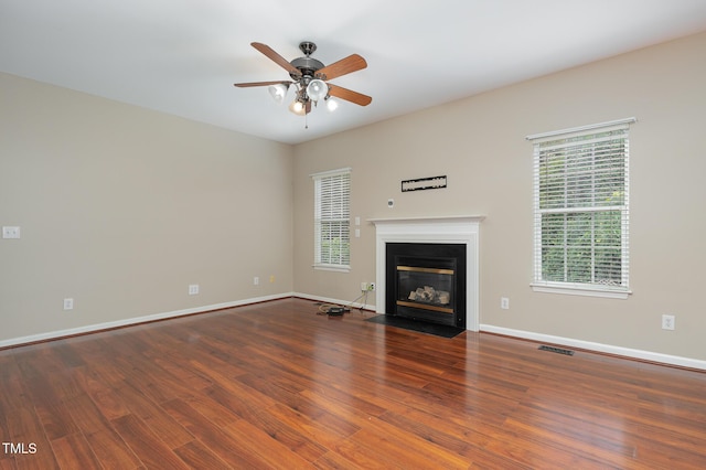 unfurnished living room with baseboards, visible vents, a fireplace with flush hearth, ceiling fan, and wood finished floors