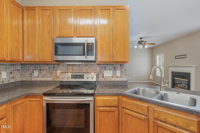 kitchen with a glass covered fireplace, ceiling fan, appliances with stainless steel finishes, a sink, and backsplash