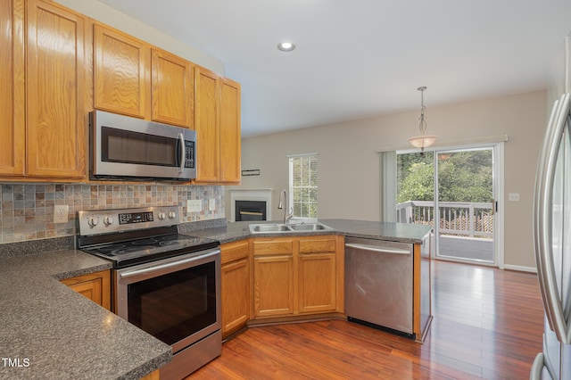 kitchen featuring stainless steel appliances, a peninsula, a sink, tasteful backsplash, and dark countertops