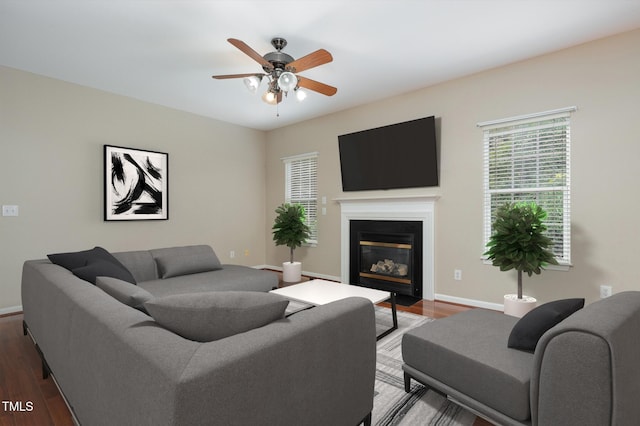 living area with a fireplace with flush hearth, ceiling fan, baseboards, and wood finished floors