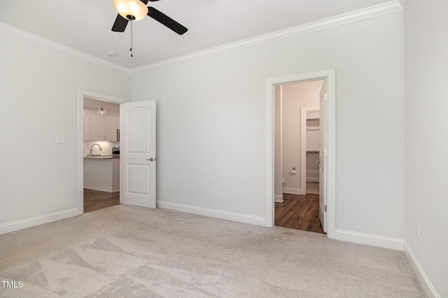 unfurnished bedroom with ceiling fan, sink, a spacious closet, light colored carpet, and ornamental molding