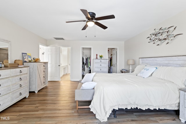 bedroom with a walk in closet, ceiling fan, wood-type flooring, connected bathroom, and a closet