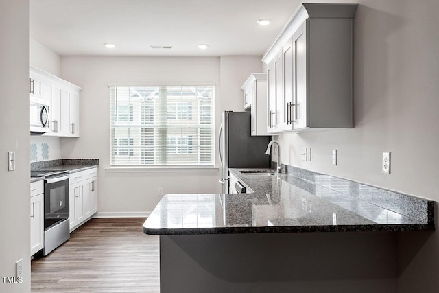 kitchen with kitchen peninsula, appliances with stainless steel finishes, sink, light hardwood / wood-style floors, and white cabinetry