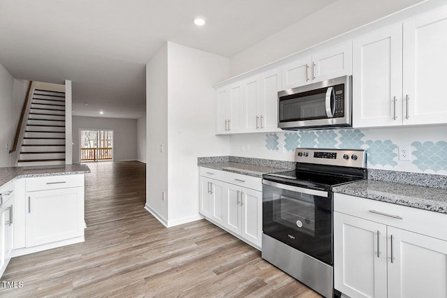 kitchen with white cabinetry, light stone countertops, light wood-type flooring, and stainless steel appliances