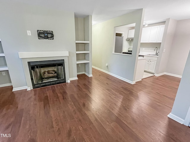 unfurnished living room featuring sink, wood-type flooring, and built in features