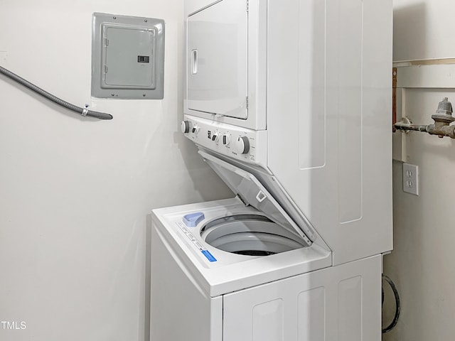 clothes washing area with electric panel and stacked washing maching and dryer