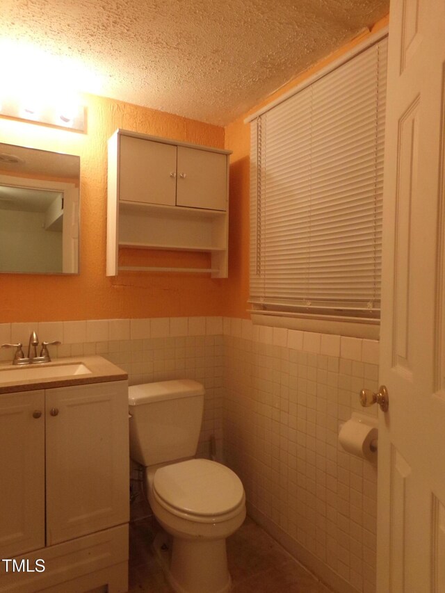 bathroom with a textured ceiling, vanity, toilet, and tile walls