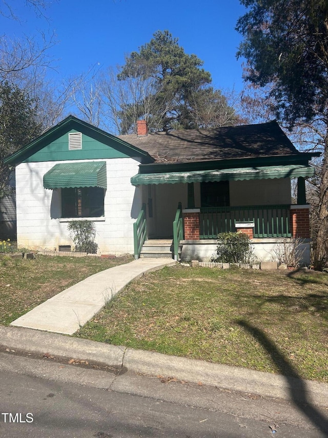 view of front of house with concrete block siding, a porch, a front lawn, and a chimney