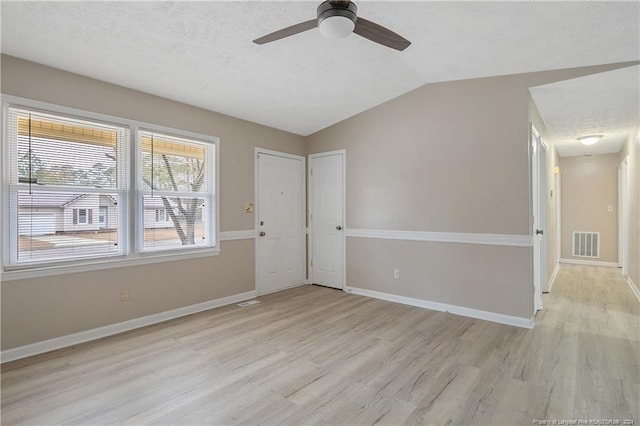 empty room with a textured ceiling, ceiling fan, lofted ceiling, and light wood-type flooring