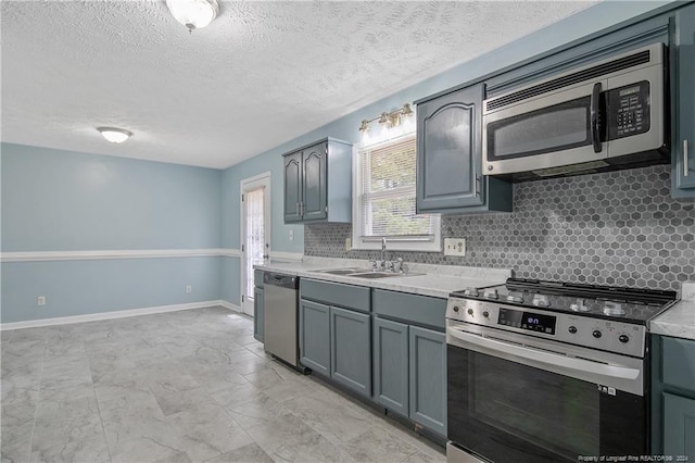 kitchen featuring sink, a textured ceiling, gray cabinets, decorative backsplash, and appliances with stainless steel finishes