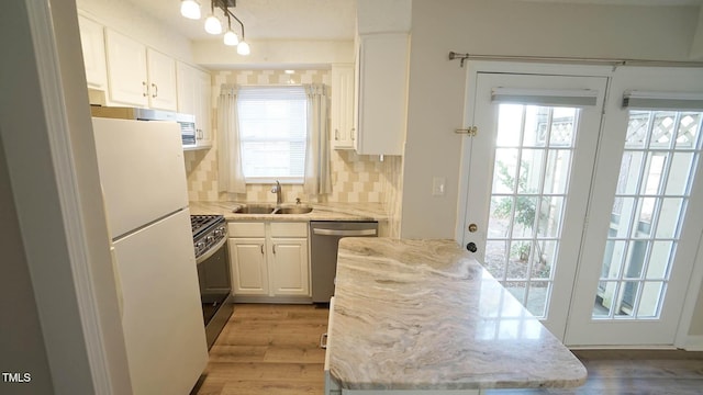 kitchen featuring white cabinetry, sink, backsplash, appliances with stainless steel finishes, and light wood-type flooring