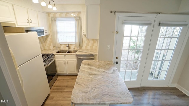 kitchen featuring sink, light wood-type flooring, tasteful backsplash, white cabinetry, and stainless steel appliances