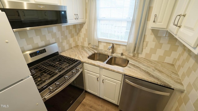 kitchen featuring sink, stainless steel appliances, light stone counters, light hardwood / wood-style floors, and white cabinets