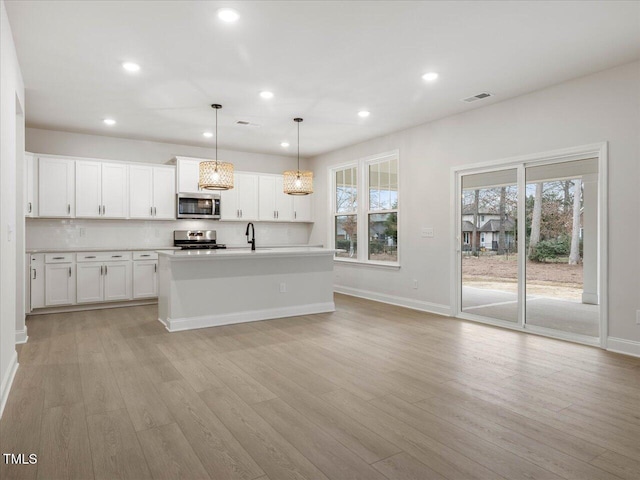 kitchen with white cabinetry, hanging light fixtures, a center island with sink, stainless steel appliances, and backsplash