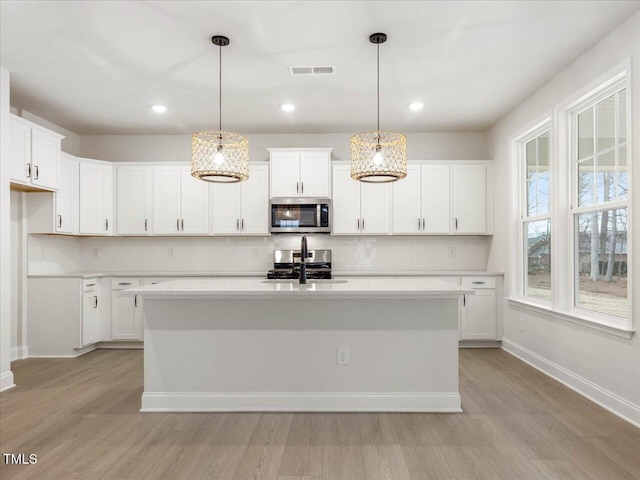 kitchen featuring pendant lighting, appliances with stainless steel finishes, a kitchen island with sink, and white cabinets