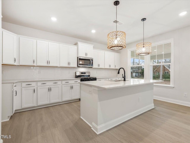 kitchen with a kitchen island with sink, sink, white cabinets, and appliances with stainless steel finishes