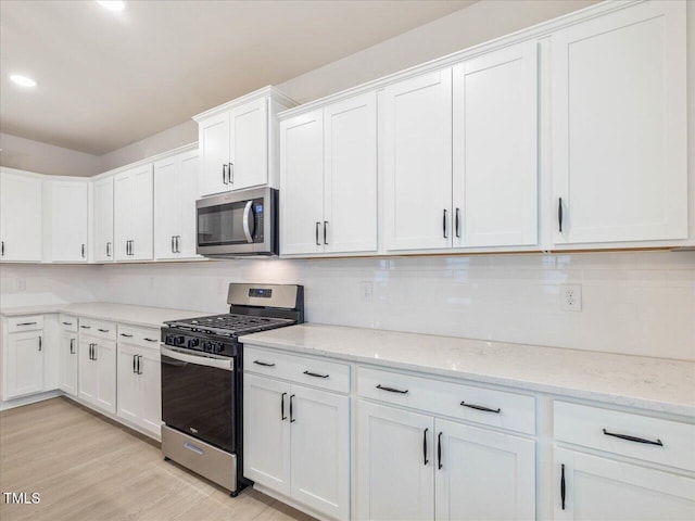 kitchen featuring appliances with stainless steel finishes, tasteful backsplash, white cabinets, light stone countertops, and light hardwood / wood-style flooring