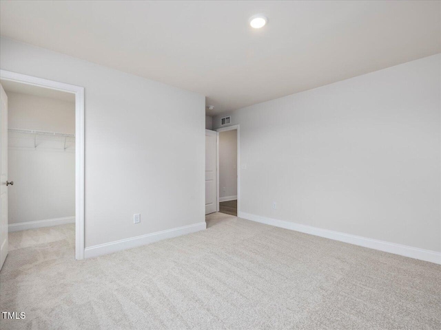 unfurnished bedroom with a walk in closet, light colored carpet, and a closet