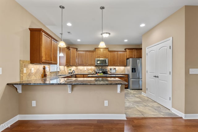 kitchen featuring pendant lighting, stainless steel appliances, dark stone counters, sink, and kitchen peninsula