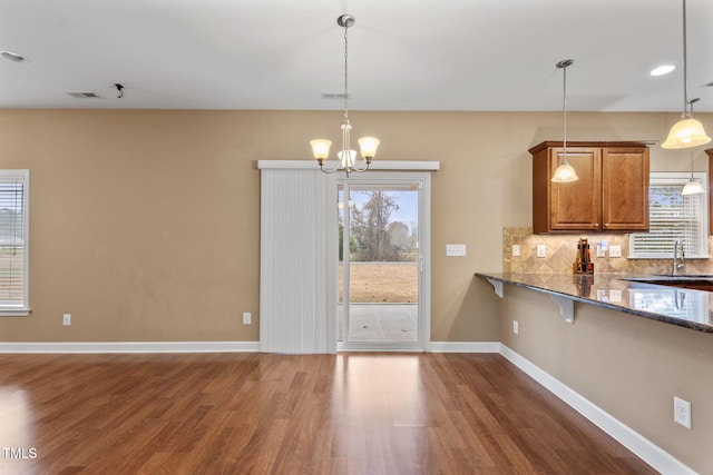 kitchen featuring decorative light fixtures, tasteful backsplash, dark hardwood / wood-style floors, dark stone countertops, and an inviting chandelier