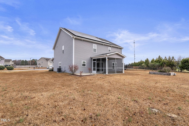 rear view of property featuring a lawn, a sunroom, and solar panels